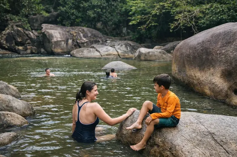 Parent and child sitting at the edge of a calm swimming hole on the El Yunque swimming tour