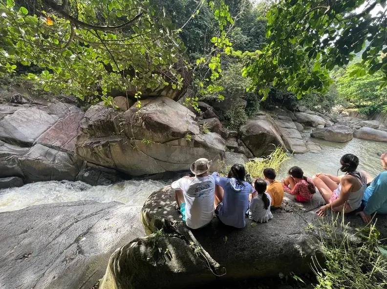 Tour group resting on river boulders beside a cascade