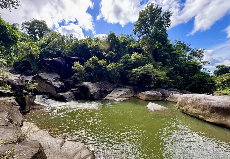 Wide, calm rainforest swimming hole framed by boulders and jungle on El Yunque's south side