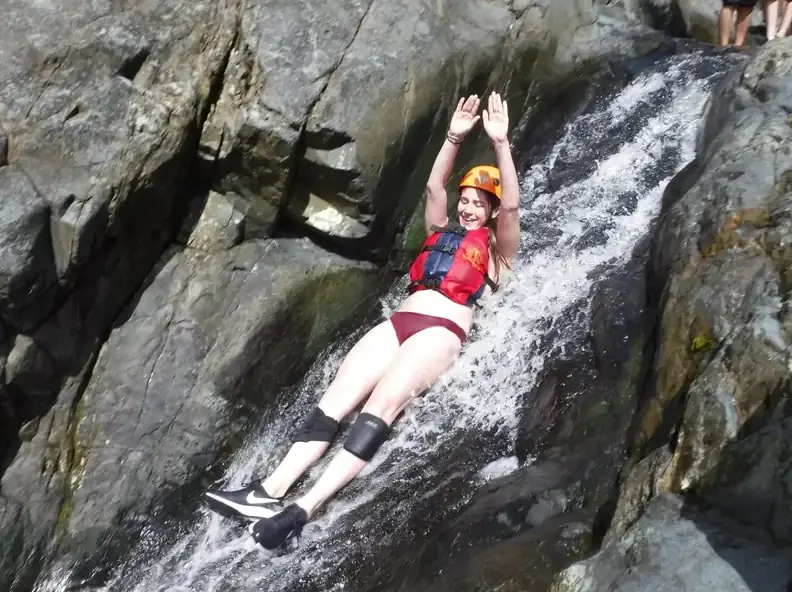 Guest with arms raised sliding down a natural waterfall slide